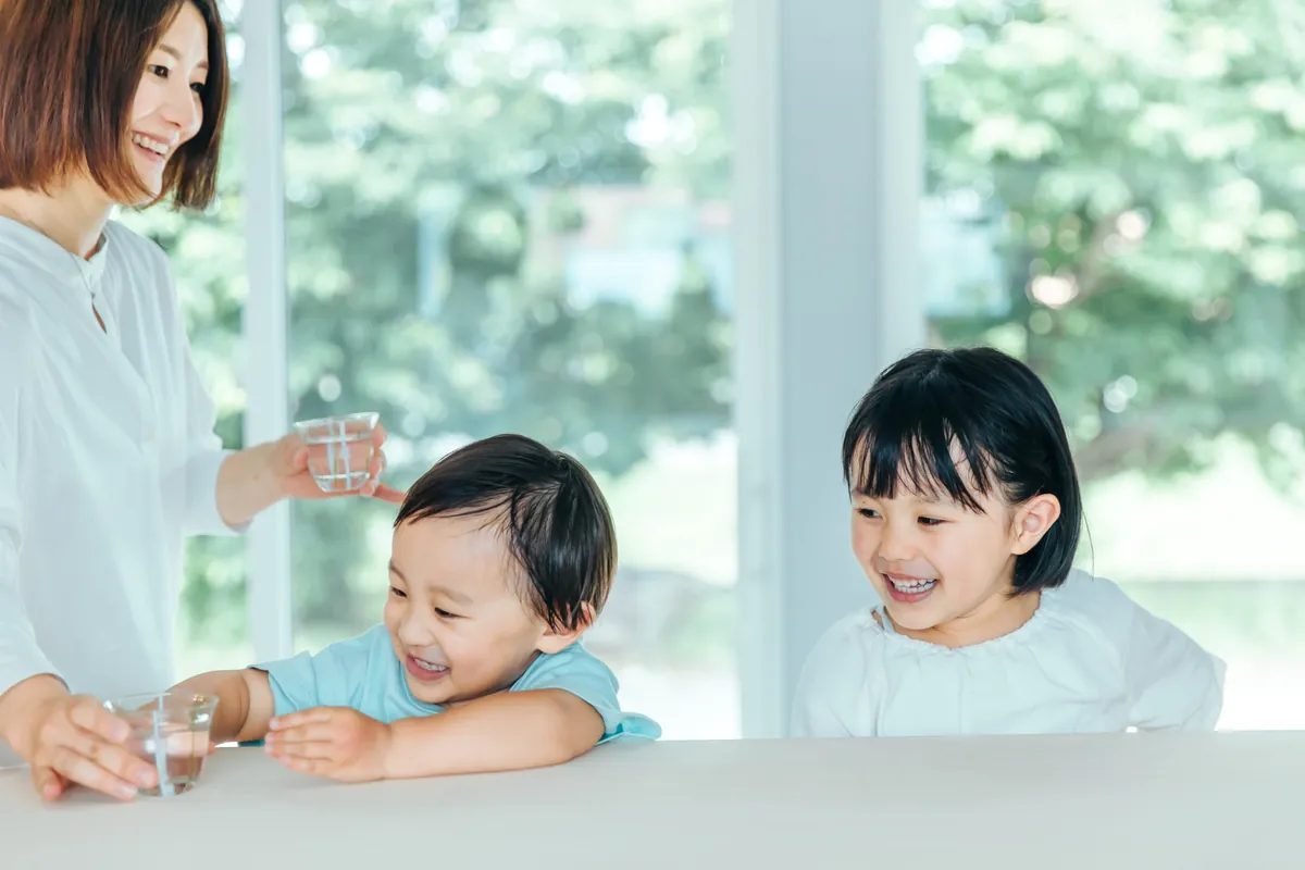 明るい窓辺でお母さんと笑う子どもたち