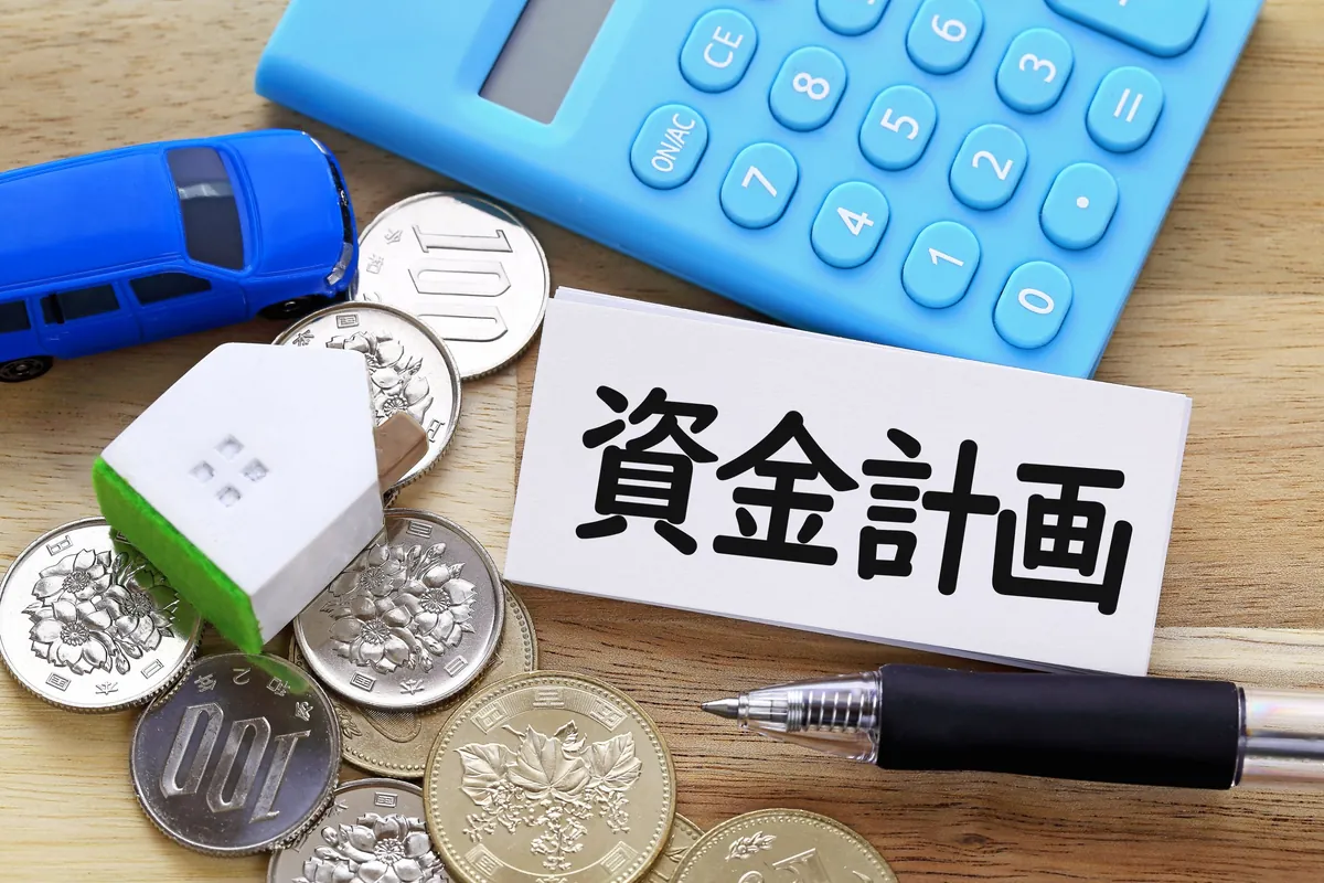 資金計画と書かれたカードと電卓、おうちの模型